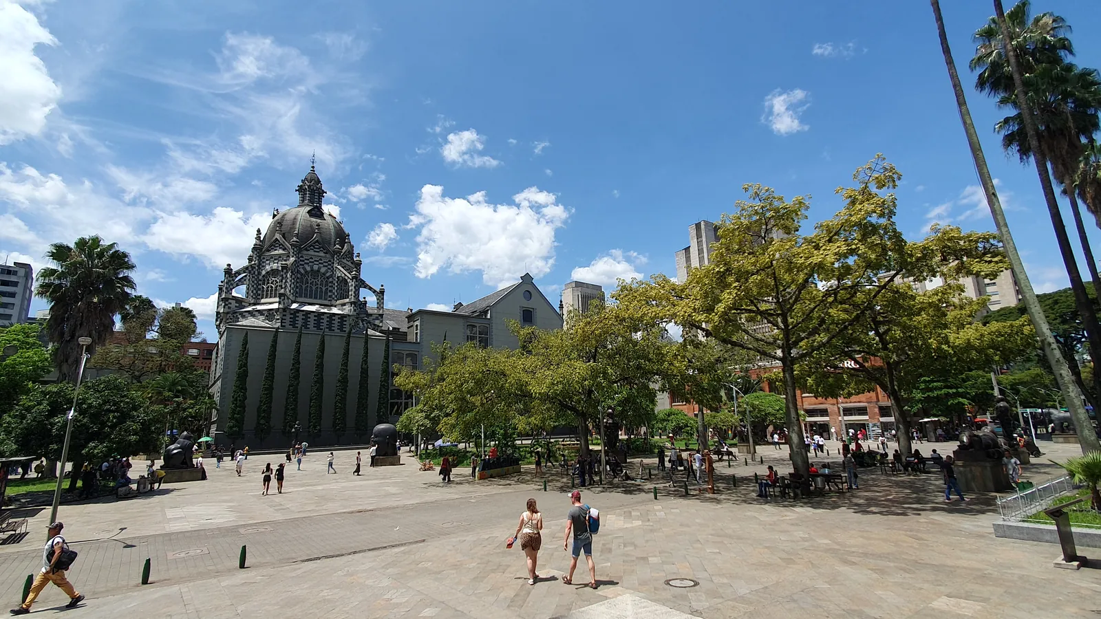 Plaza Botero in central Medellín on a sunny day, with palm trees and the Palacio de la Cultura